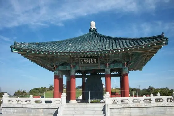 A large bell in the middle of a park.